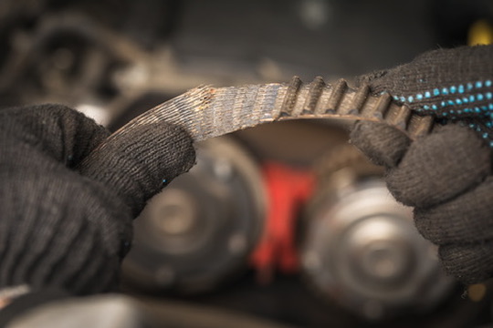 an auto mechanic removed a torn timing belt with worn teeth from a car, close up